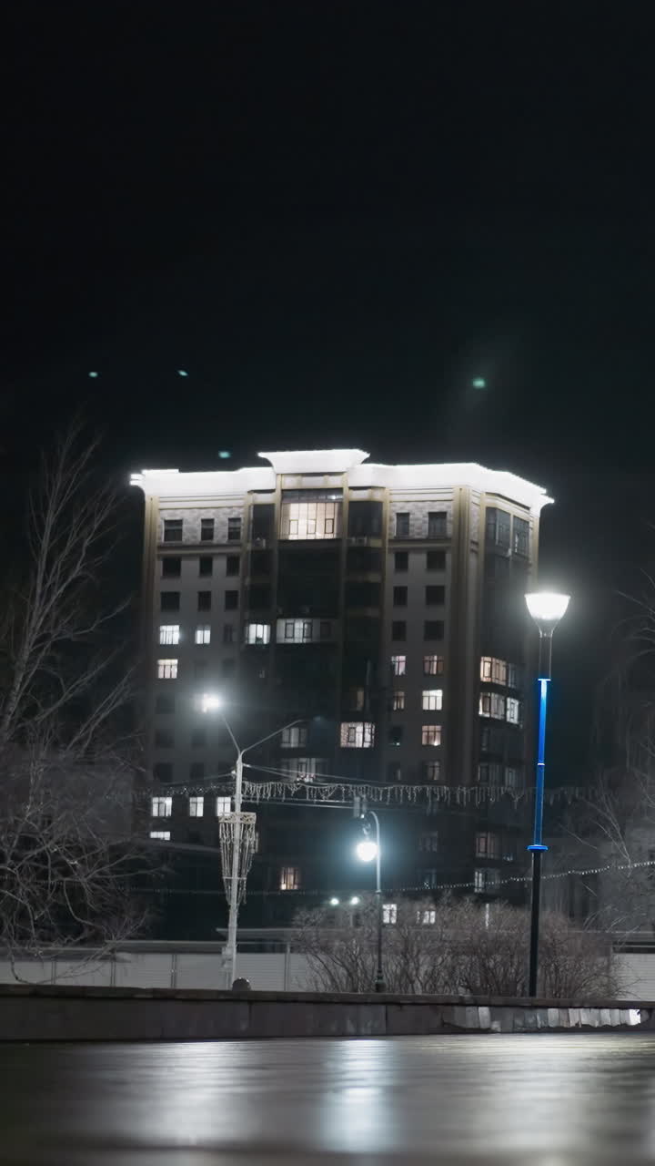 vista nocturna de personas caminando por una zona urbana iluminada, con farolas y un edificio de gran altura en el fondo