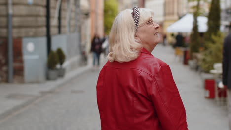 Rear-view-of-senior-woman-tourist-walking-through-the-street-outdoors,-looking-searching-for-a-way