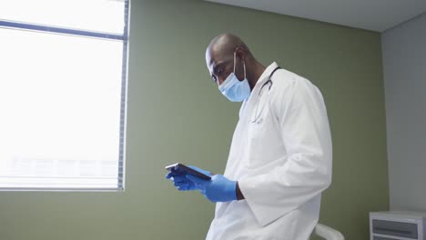 médico afroamericano de alto rango que usa una máscara facial usando una tableta digital en el hospital