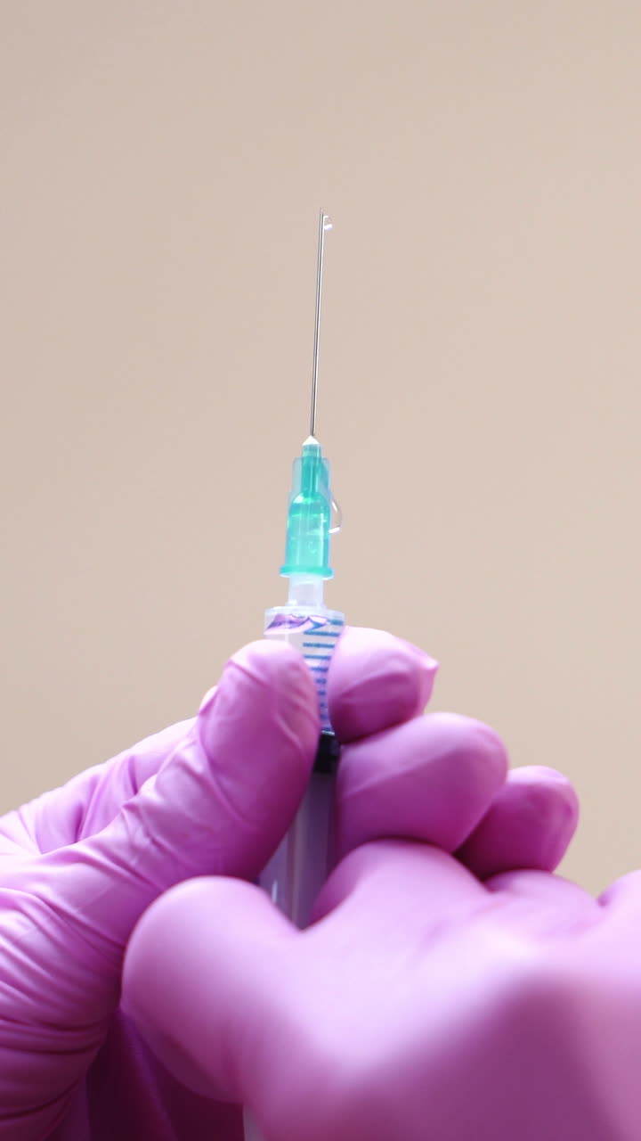 Close-up view on a cosmetologists hands in gloves holding syringe with needle for rejuvenating facial injections. Vertical video