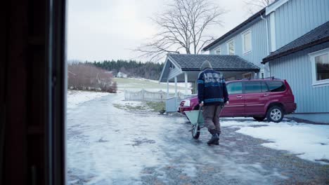 a man is pushing a wheelbarrow along an icy road to transport materials required for the diy hot tub - static shot