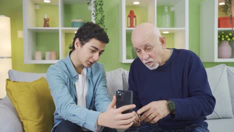 Cheerful-grandson-teaching-his-grandfather-how-to-use-a-phone.