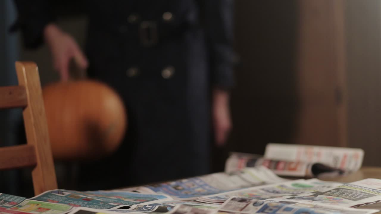 Una persona che appoggia una zucca sul tavolo coperto di giornali - Primo piano
