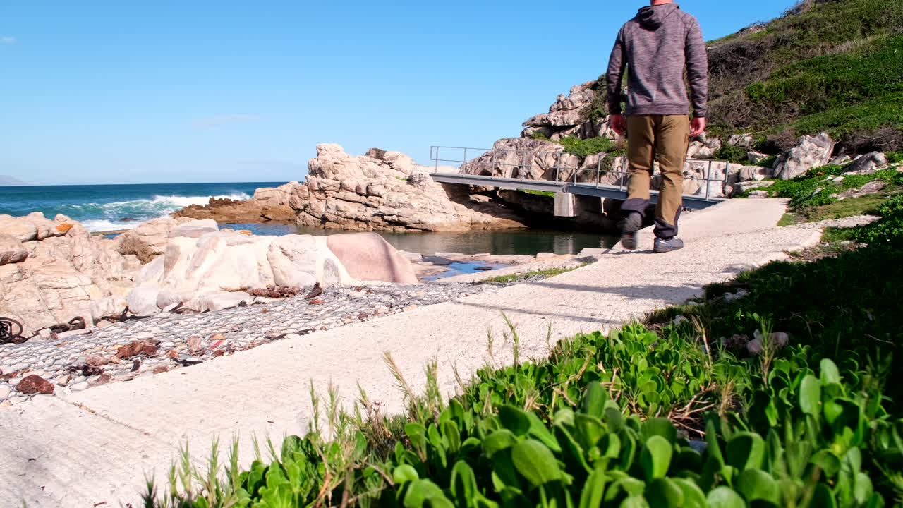 Man strolls on scenic coastal cliff path next to ocean, ecotourism concept