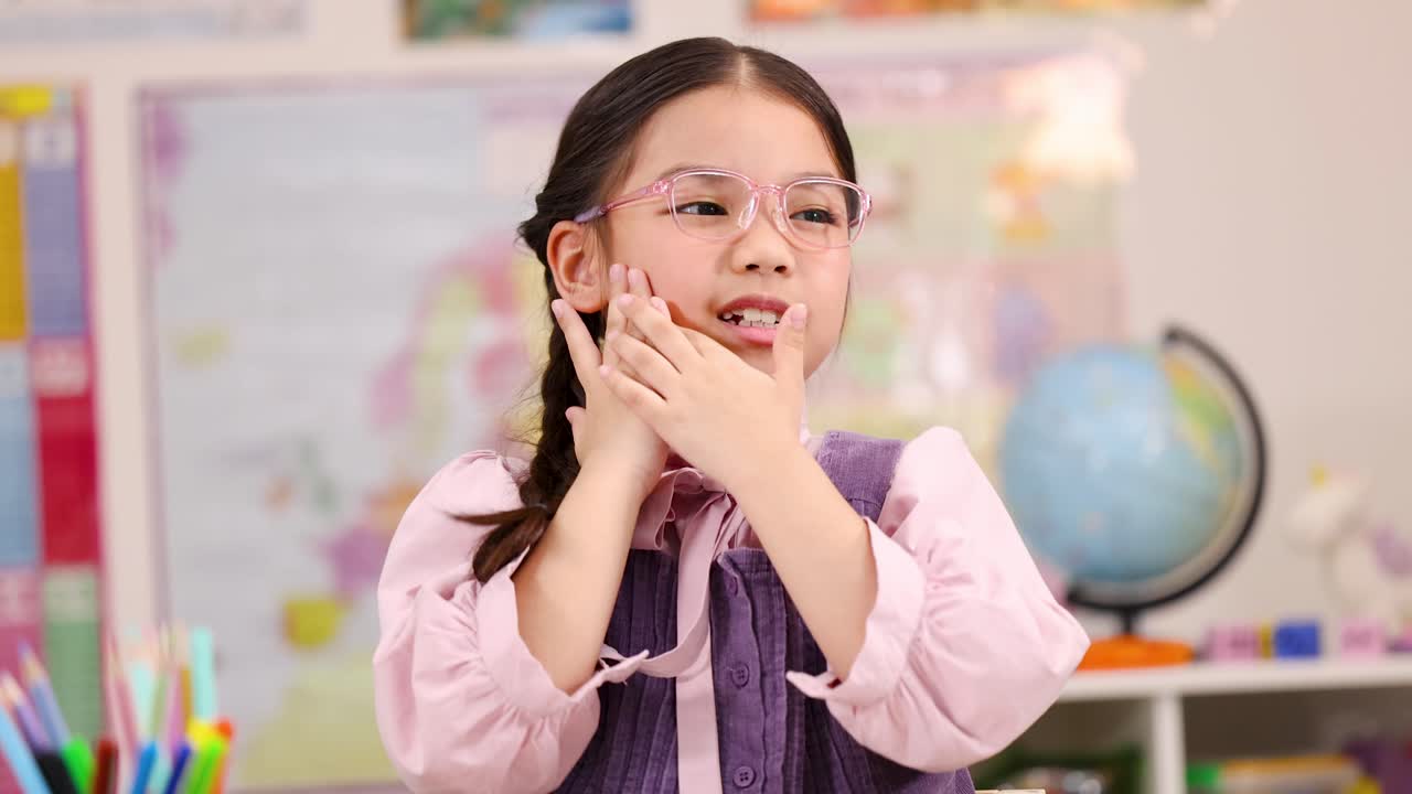 Asian schoolgirl with pink glasses suffers toothache in bright classroom, static medium shot