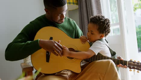 Vorderansicht-Eines-Jungen-Schwarzen-Vaters-Und-Eines-Kleinen-Sohnes,-Der-Im-Wohnzimmer-Des-Komfortablen-Zuhauses-4-Gitarre-Spielt