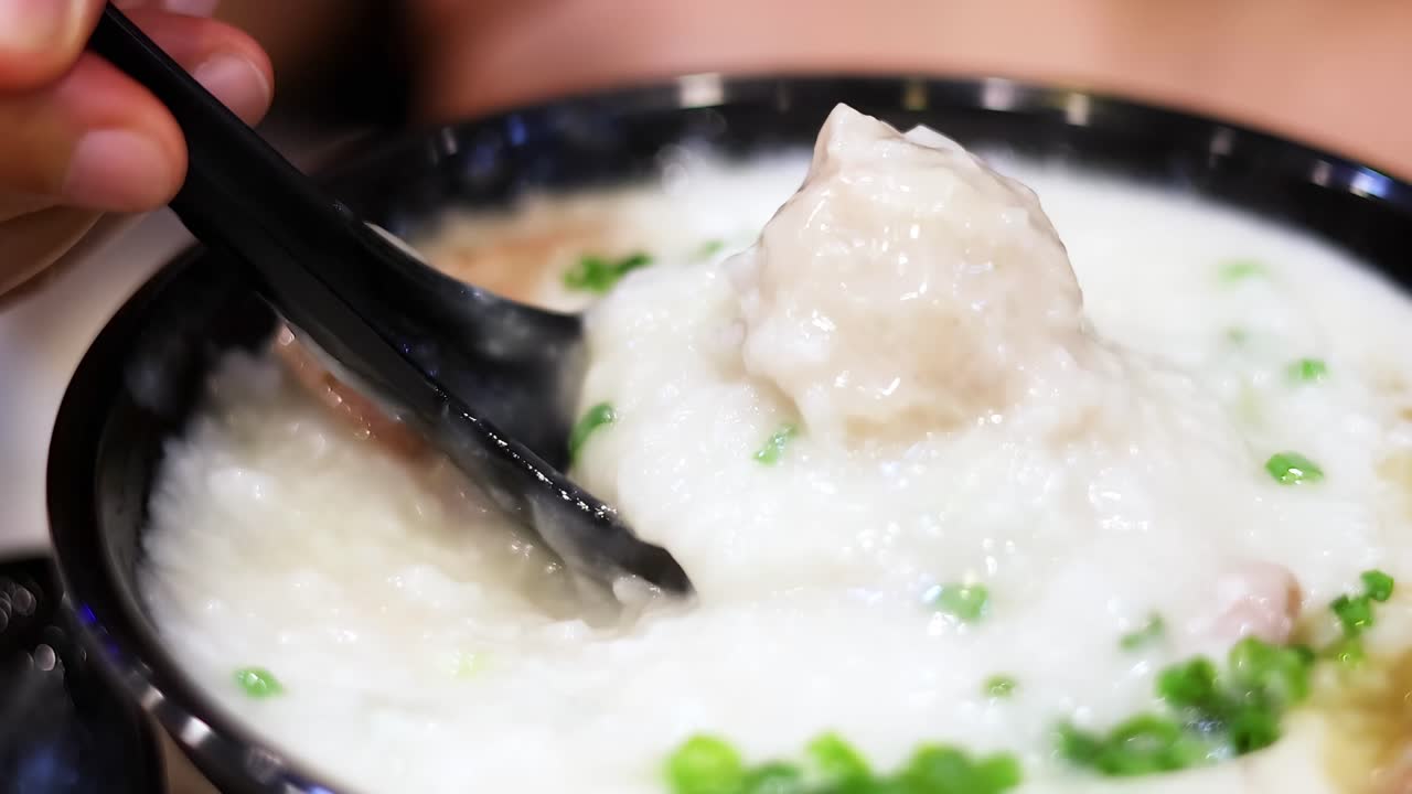 Tampilan dekat sendok yang mengangkat bubur nasi lezat dengan daun bawang dan daging