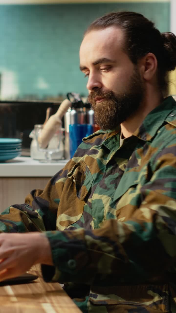 Video verticale. Soldato in uniforme militare che si gode una colazione tranquilla con caffè fresco e laptop.
