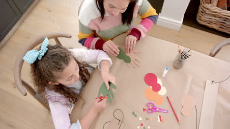 happy biracial mother and daughter cutting and sticking cutouts in sunny living room