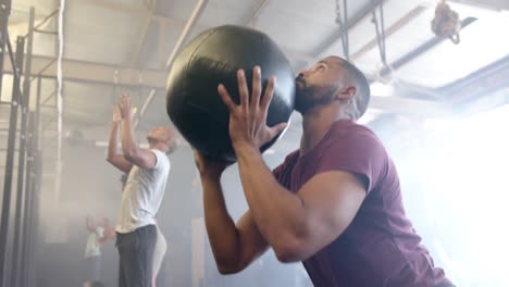 diverse group fitness class training at gym lifting and throwing medicine balls, in slow motion