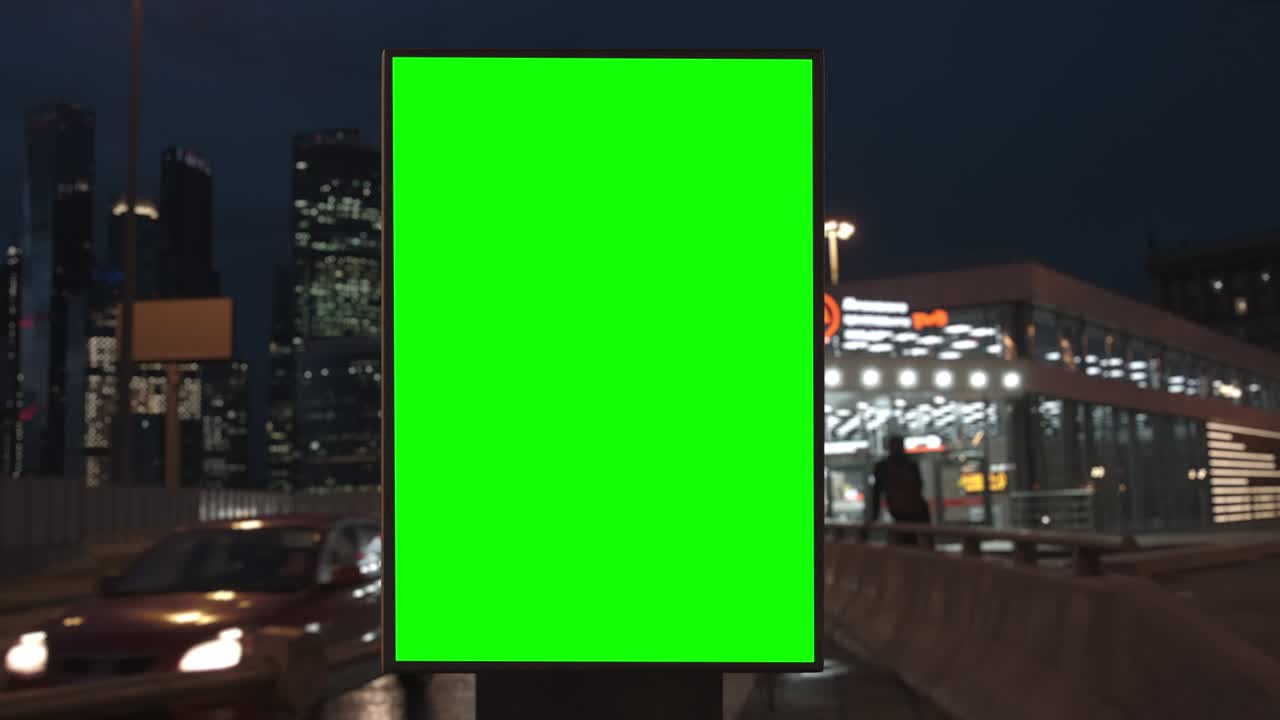 Cartellone pubblicitario con schermo verde su un'autostrada trafficata con traffico, luci al neon