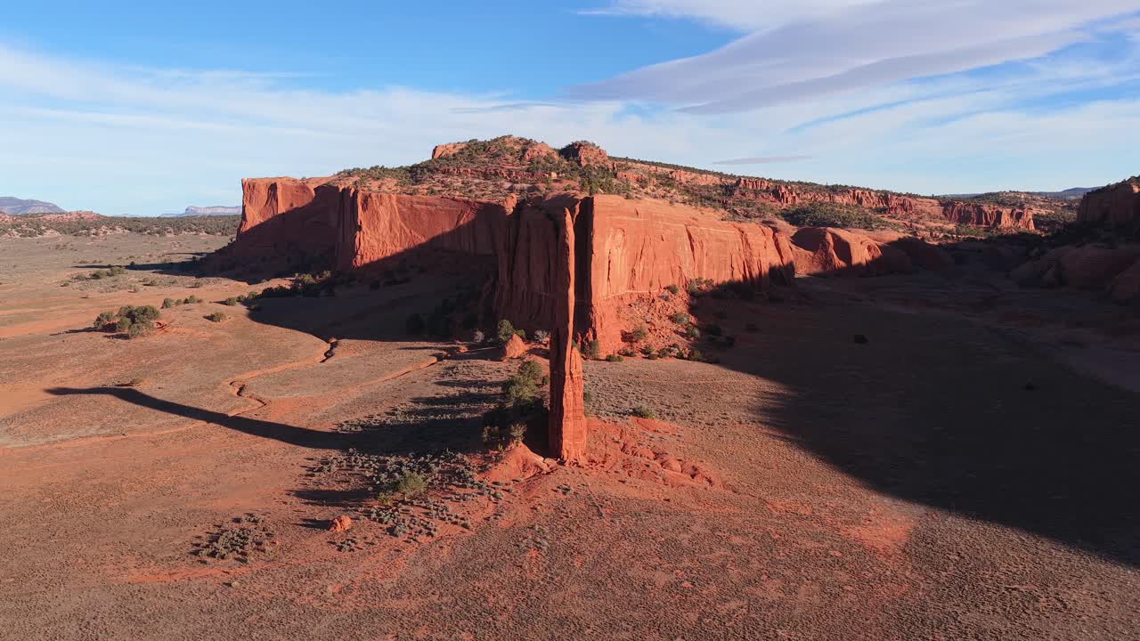 Un'orbita lenta e fluida del drone circonda un silenzioso pinnacolo di roccia rossa, catturando la tranquilla solitudine e la presenza imponente di questo antico monolito geologico in un vasto paesaggio desertico arido