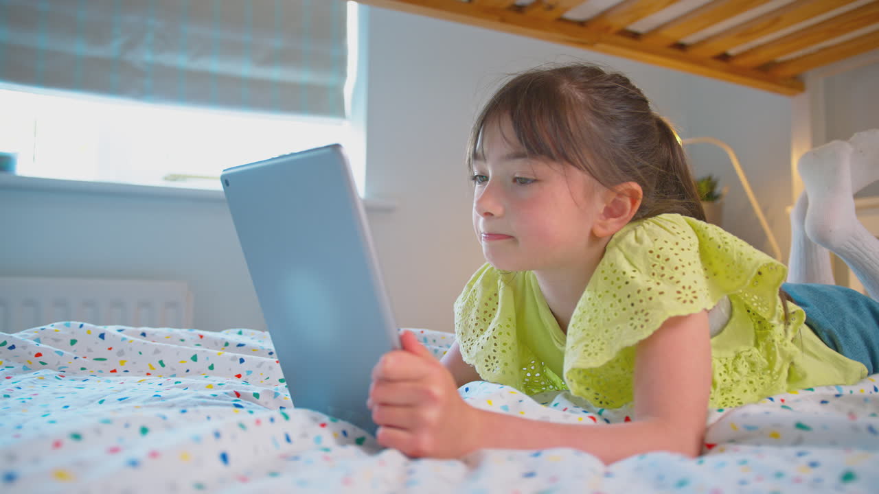 chica en el dormitorio en casa acostada en la cama usando una tableta digital