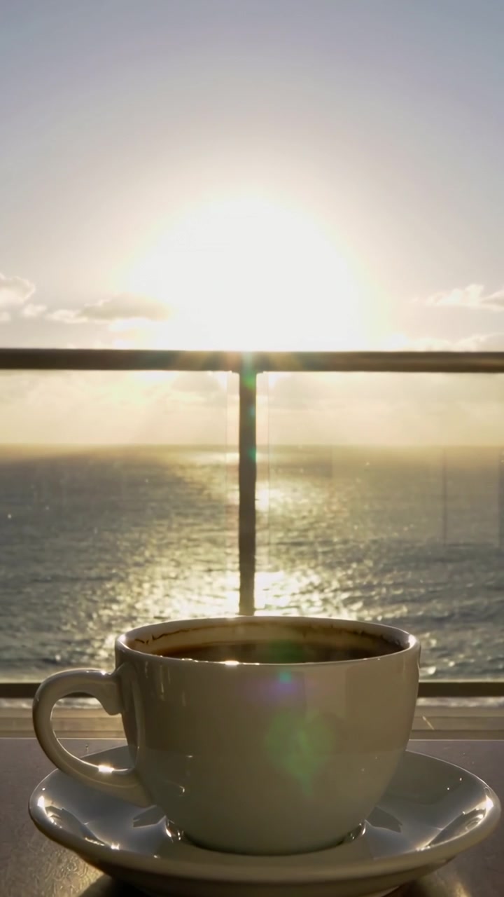 Video verticale: Sole nascente che proietta riflessi scintillanti sul mare da un balcone, tazza che mostra un bagliore dell'obiettivo
