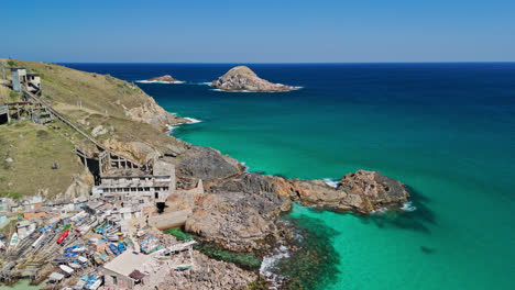 ramshackle wooden homes and broken boats gather in clear turquoise green waters on edge of rocky beach below brooken home and observation deck