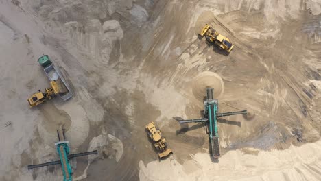 Top-aerial-view-of-bulldozer-loading-sand-into-empty-dump-truck-in-open-air-quarry