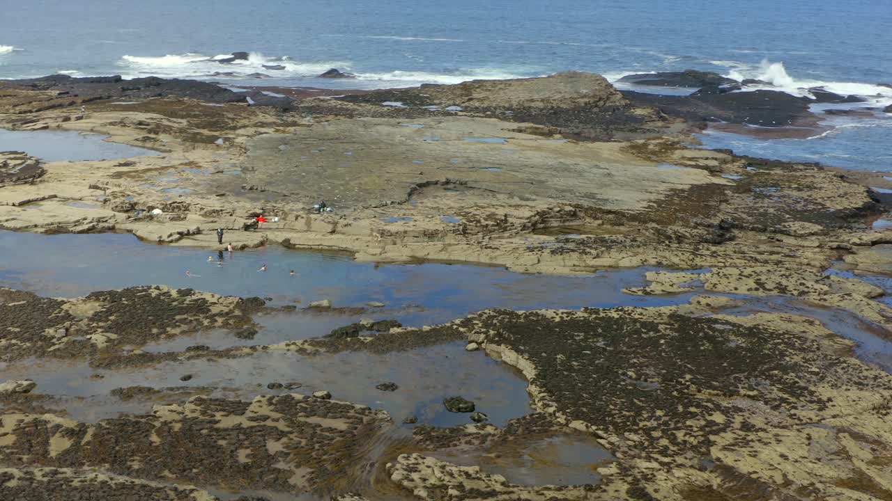 Aerial shot of Pollock Holes in Kilkee, showcasing natural pools filled with swimmers enjoying the beautiful weather