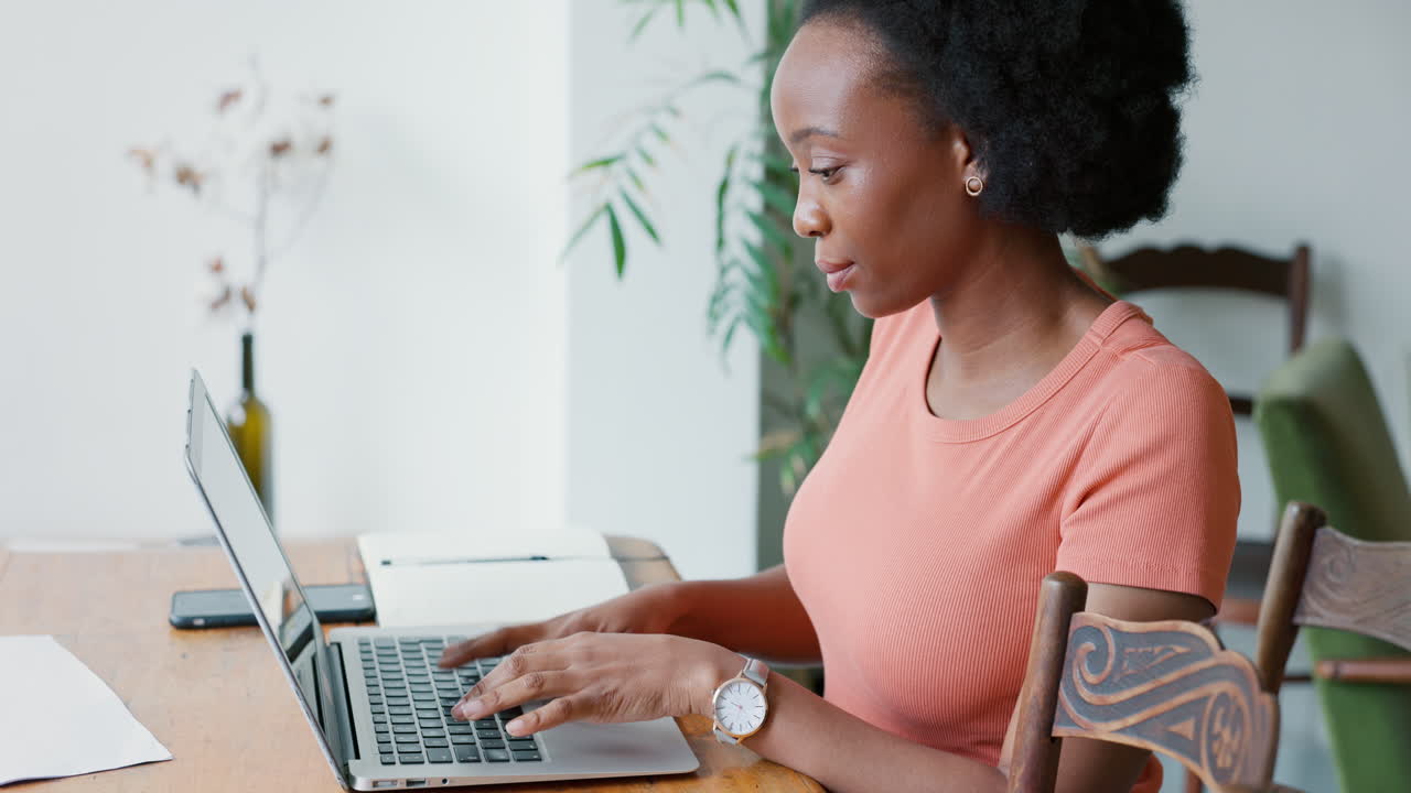 Black freelancer typing on a laptop in her dining