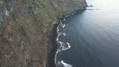 aerial footage of canary island rocky cliff and large waves washing a black beach in la palma, canary islands