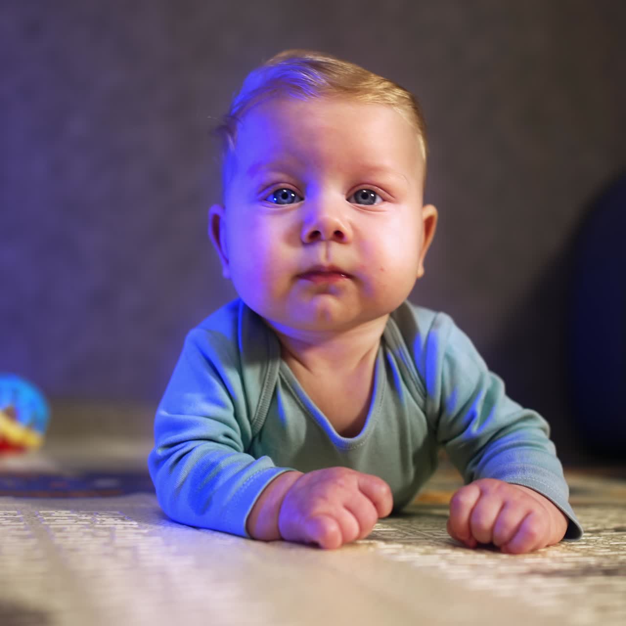 Bebê adorável com bochechas rechonchudas deitado no chão. Criança calma olhando para frente com interesse. Plano de fundo desfocado