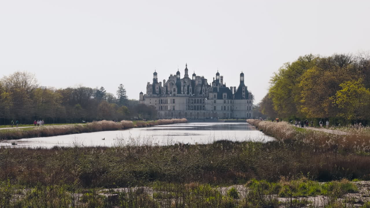 Chambord castle view with canal, spring trees, tourists, peaceful and historic vibe
