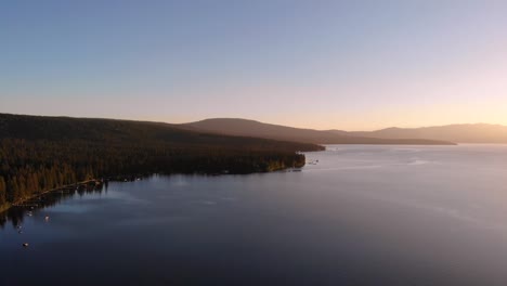 Drone-shot-sliding-to-the-right-while-flying-over-a-lake-with-a-glowing-sunset-over-the-horizon