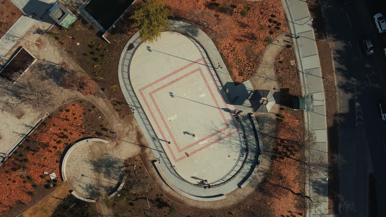 antena de arriba hacia abajo girando sobre personas patinando en pista en parque público otoñal en los dominicos, santiago, chile