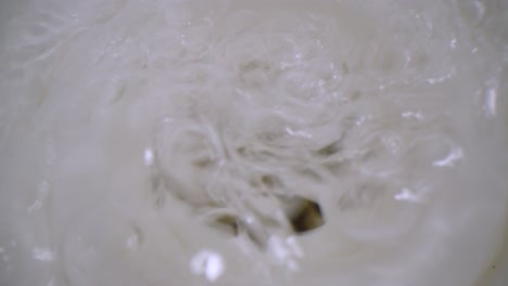 macro close up of a bathtub plug hole as water turned on hard to aggressively bubble around and run down the hole