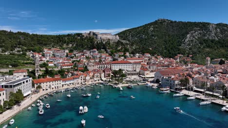 backward dolly out aerial view of hvar island bay, overlooking luxury cruise ship, boats, yachs and španjola fortress
