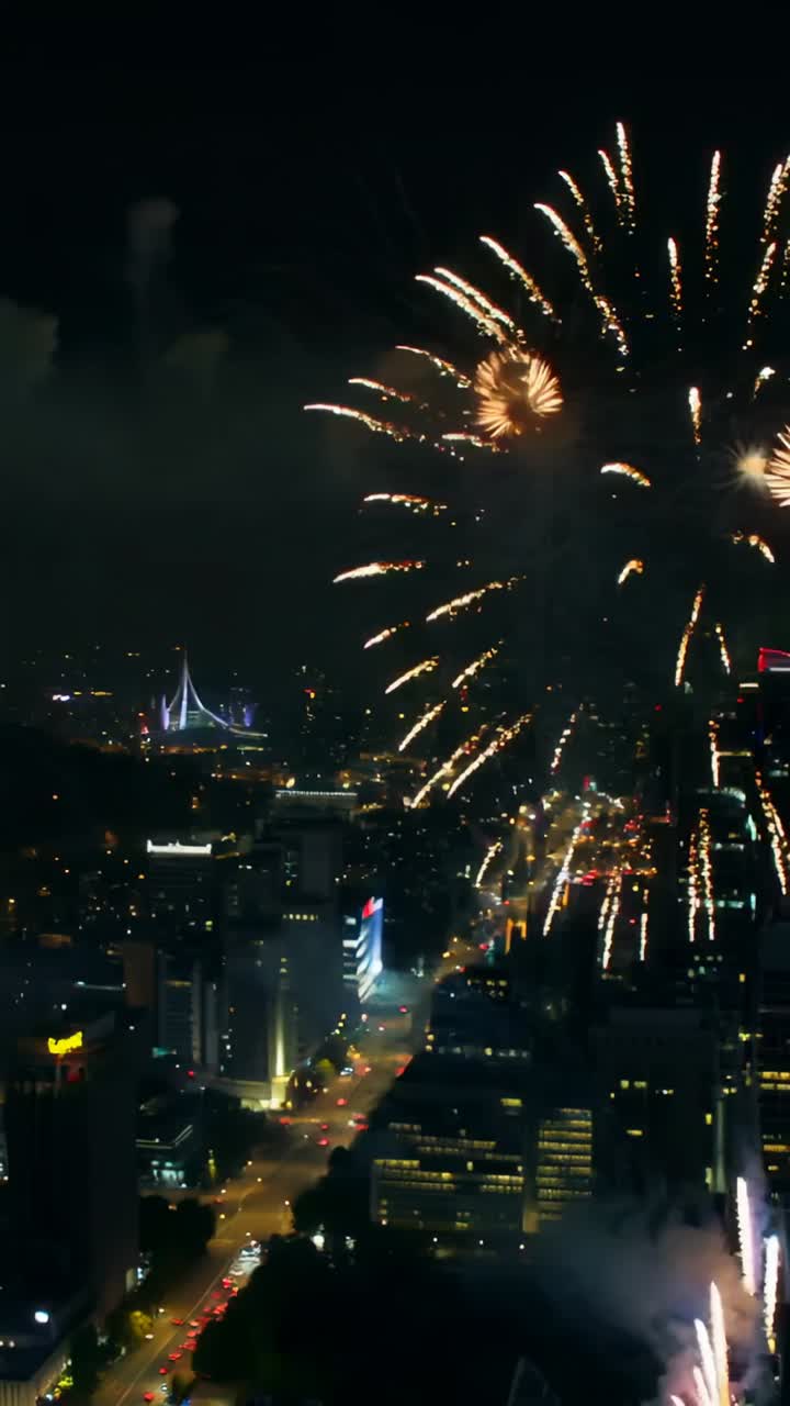 Vertical video: Launching fireworks shells over downtown bursting red blue bursts lighting rooftops