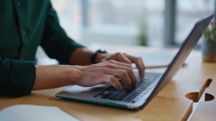 Nahaufnahme eines Geschäftsmannes, der in einem Büro einer Kreativagentur eine E-Mail auf einen Laptop schreibt