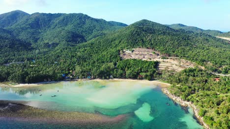 Beautiful-shoreline-of-tropical-island-with-coral-barriers,-turquoise-shallow-lagoon-and-rocks-under-green-sharp-slopes-of-hills-in-koh-phangan,-Thailand