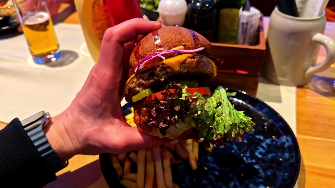 Primer plano de una mano sosteniendo una deliciosa hamburguesa con lechuga fresca e ingredientes en un plato