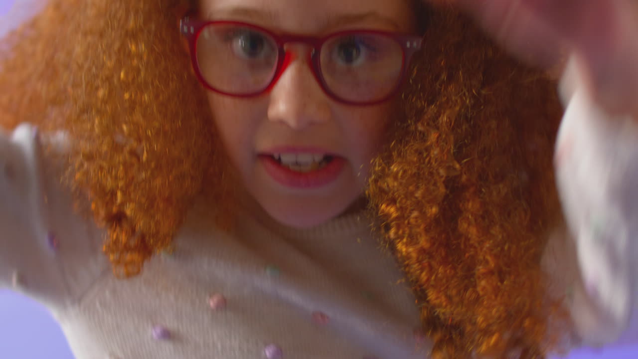 빨간 안경을 입은 활기찬 소녀가 보라색 배경에서 점프하고 춤을 추는 스튜디오  ⁇