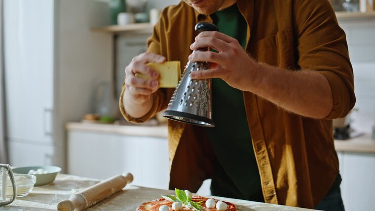 Primo piano di pizzaiolo che aggiunge foglie di basilico fresco a una pizza fatta in casa in cucina