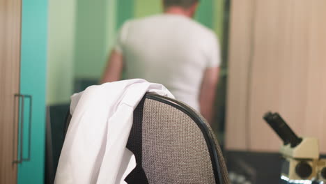 close-up view of a scientist placing a lab coat on the back of a chair in a laboratory, and walking away