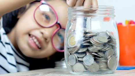 asian little girl putting the coin in to a glass jar shallow depth of field select focus on jar