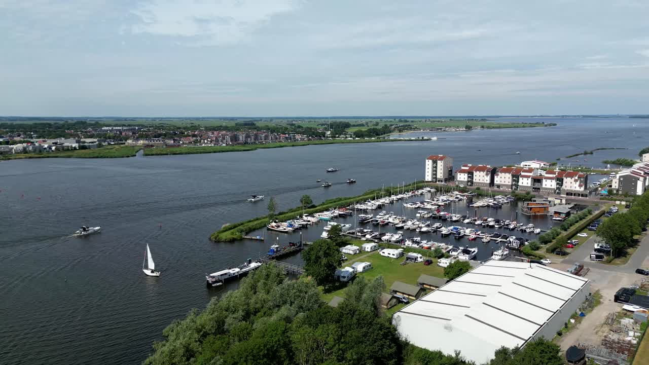 Lively harbor scene with sailboats and yachts docked along a calm river under a bright summer sky.