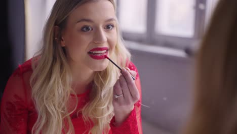 woman applying red lipstick in front of a mirror