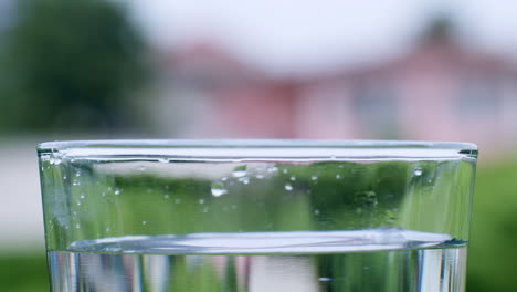 Tiny-droplets-splashing-in-a-glass-filled-with-mineral-water,-creating-ripples-and-waves-near-its-rim