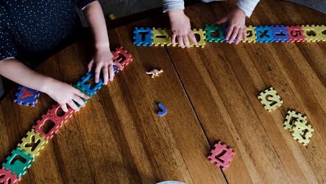 twins building and playing with foam puzzle, top-down view of hands in play on wooden table