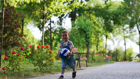 happy smiling child with a ball running in the park. active baby boy throws the ball on the road.
