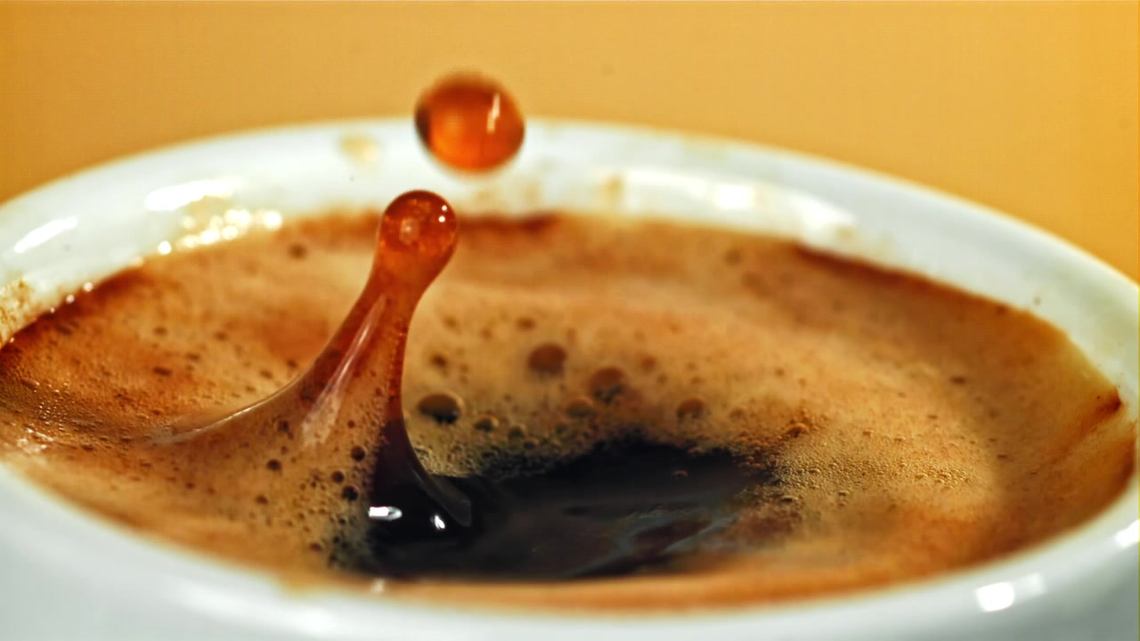 Gocce di caffè al rallentatore che schizzano in una tazza bianca