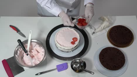 chef placing sliced strawberries on layer of cake that already has some cream on top.