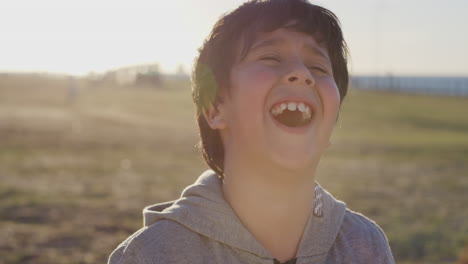 close up portrait young hispanic boy laughing cheerful playful kid enjoying summer vacation on seaside park sunset