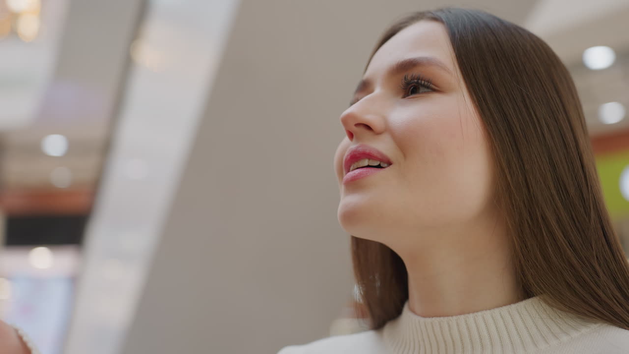 Close-up of young lady smiling as she smells decorative Christmas tree with a sign of satisfaction, background features festive decorative lights creating a joyful, holiday shopping atmosphere