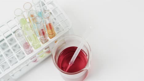 Coloured-liquid-in-flask-with-test-tubes-in-stand-on-white-background-with-copy-space,-slow-motion