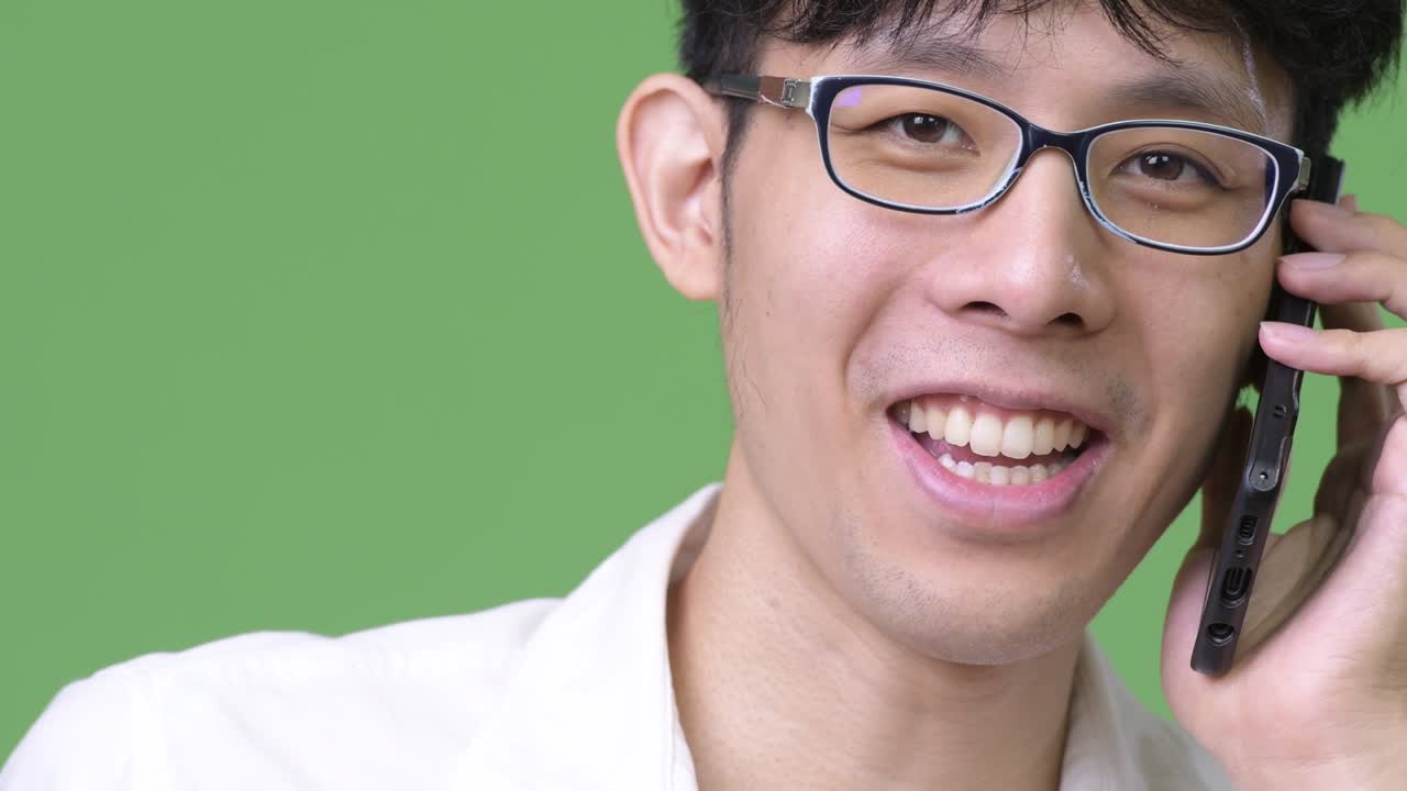 행복 한 젊은 아시아 사업가 가 전화 를 하면서 미소 짓고 있다