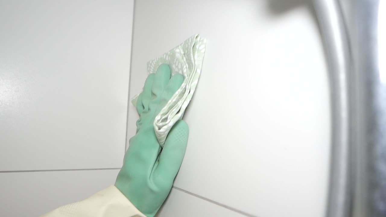 Hand in rubber glove cleaning white tiled surface