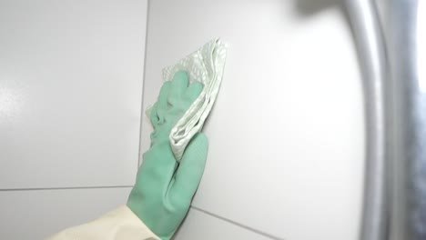 hand in rubber glove cleaning white tiled surface